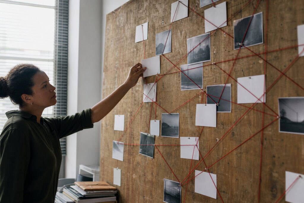 A researcher pins a blank index card onto a wooden evidence board strung with red thread connecting other cards.