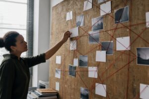 A researcher pins a blank index card onto a wooden evidence board strung with red thread connecting other cards.
